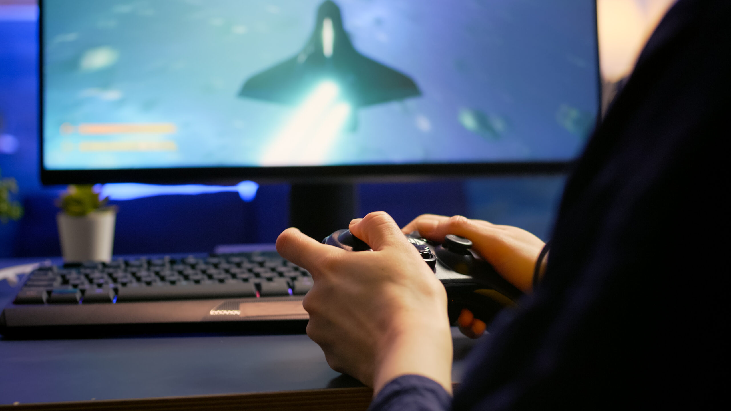 Close-up of professional cyber gamer playing space shooter video game using wireless controller. Pro player use RGB equipment during gaming tournament late at night in home studio