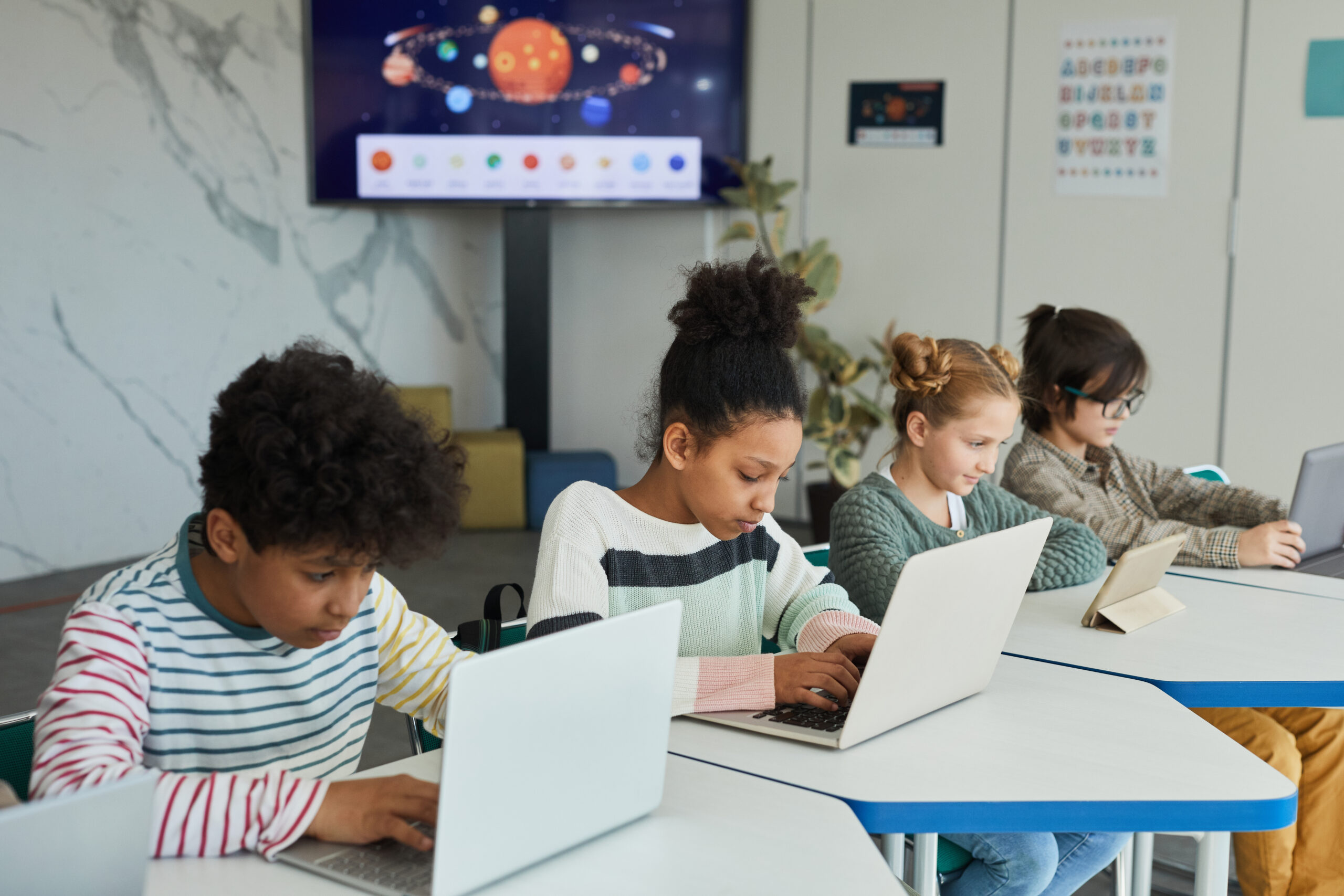 Diverse group of children sitting in row at school classroom and using computers